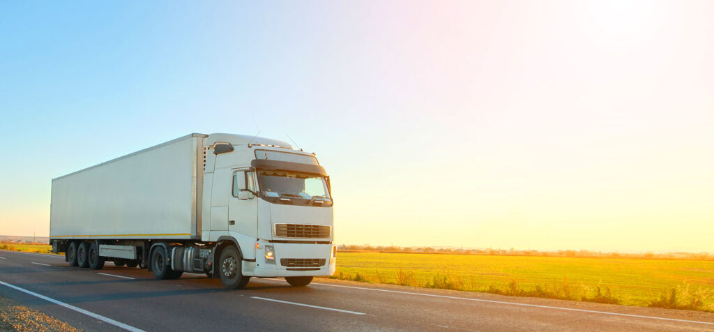 White semi-truck with refrigerated trailer driving on highway at golden hour