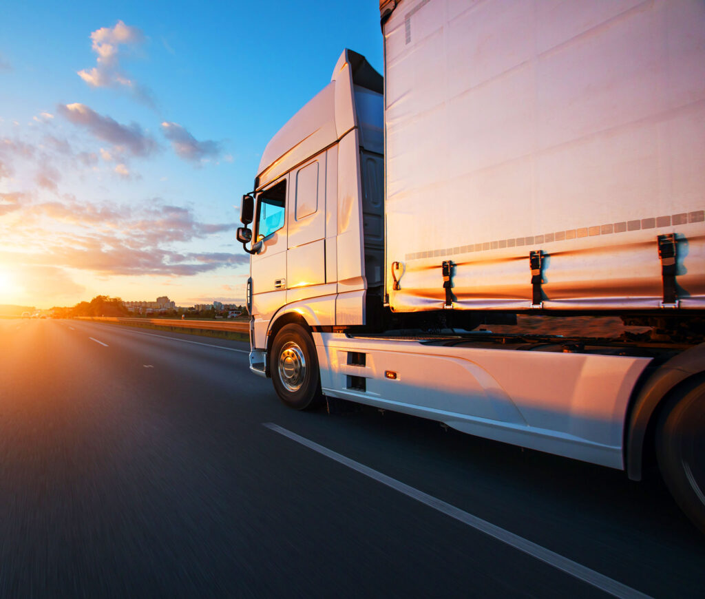 White semi-truck with cargo trailer speeding on freeway at sunset