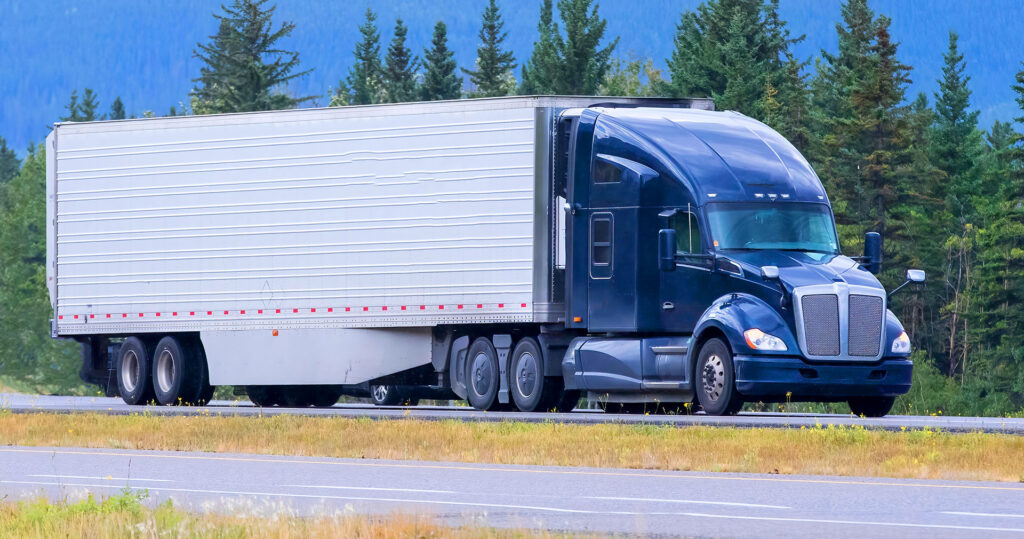Blue semi truck hauling trailer on forest highway