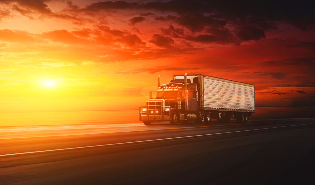 Semi truck driving on coastal highway during dramatic sunset