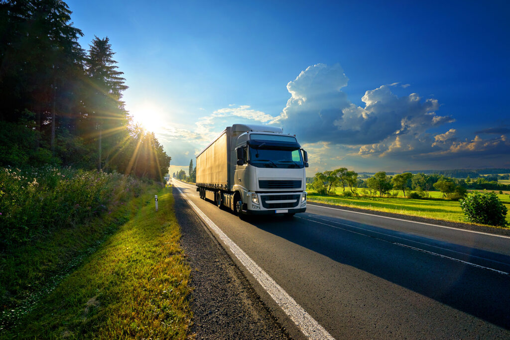 White semi truck driving highway at sunset with cargo trailer