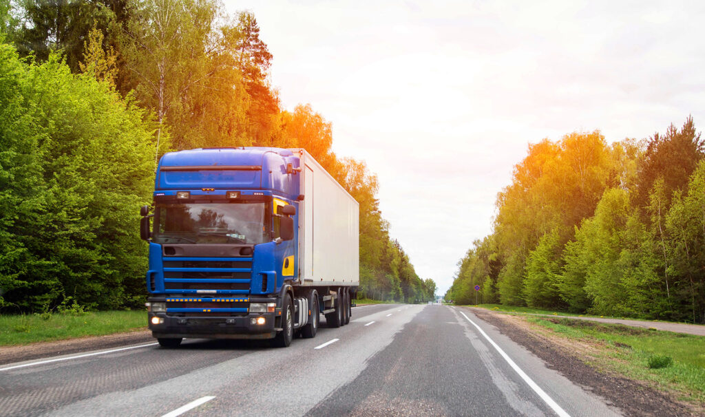 Blue semi truck hauling cargo trailer on tree lined highway